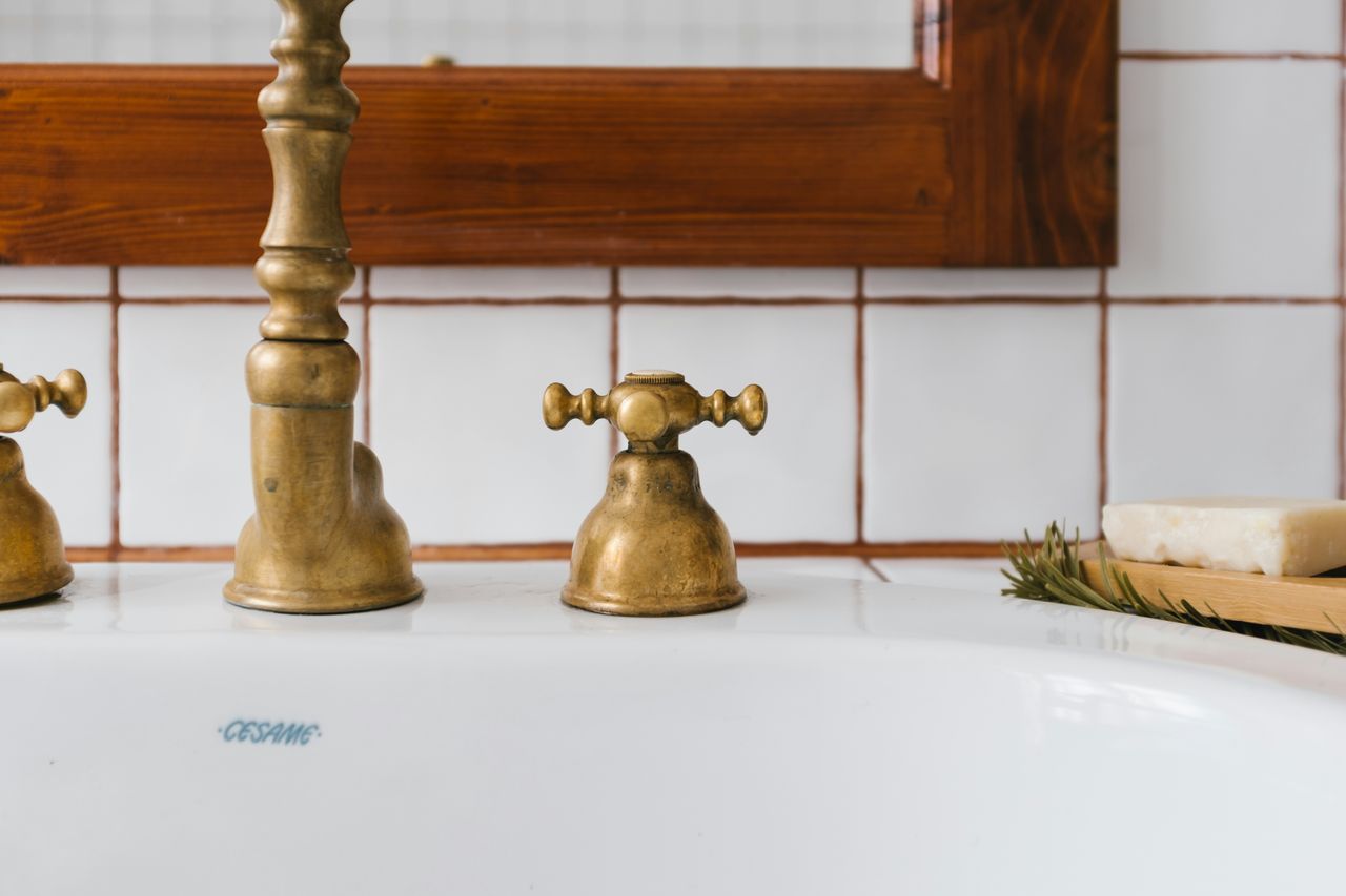 Brass faucet above a white ceramic basin beside bamboo and soap